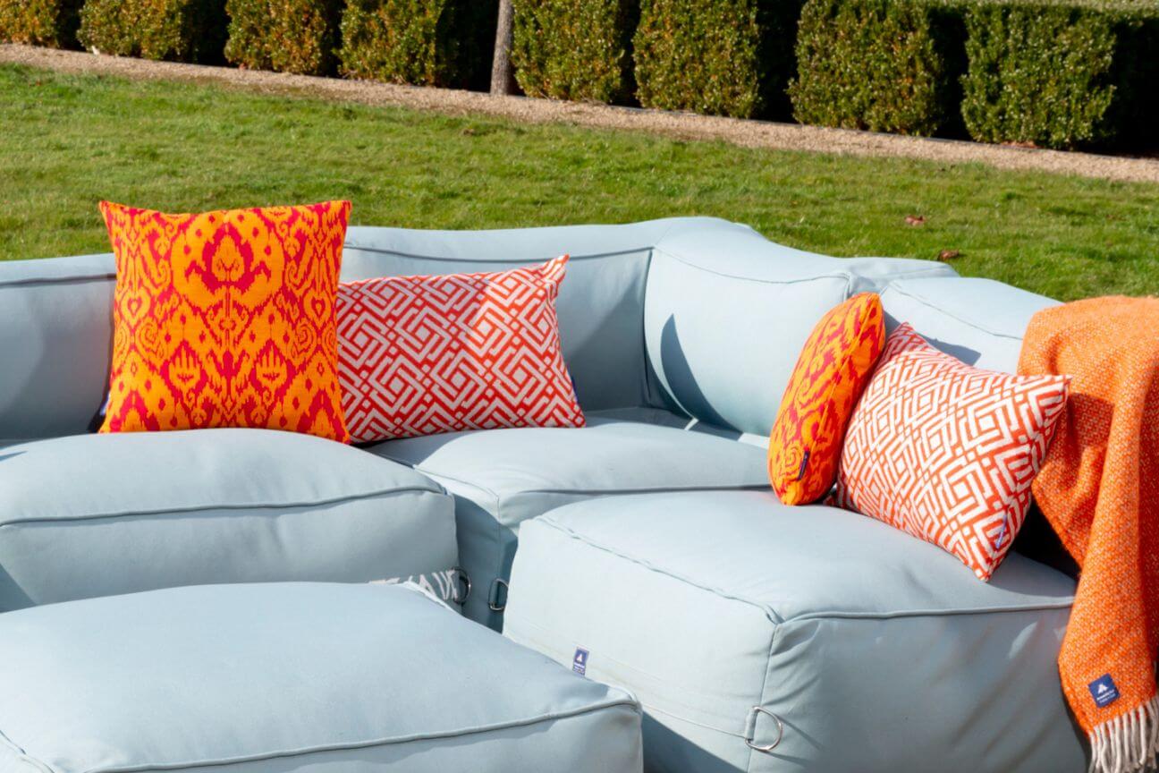 Modular garden sofa outdoors on a hot and sunny day, covered in orange cushions