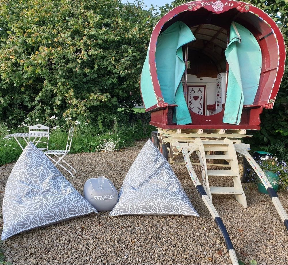 Two comfy-looking bean bag chairs on gravel next to a wooden gypsy caravan.