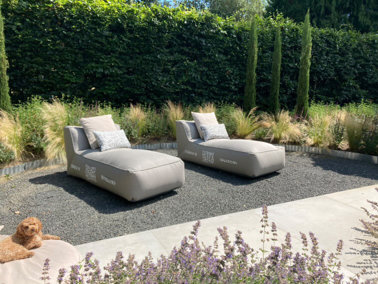 Two luxury cushioned sun loungers on a gravel patio in the sunshine.