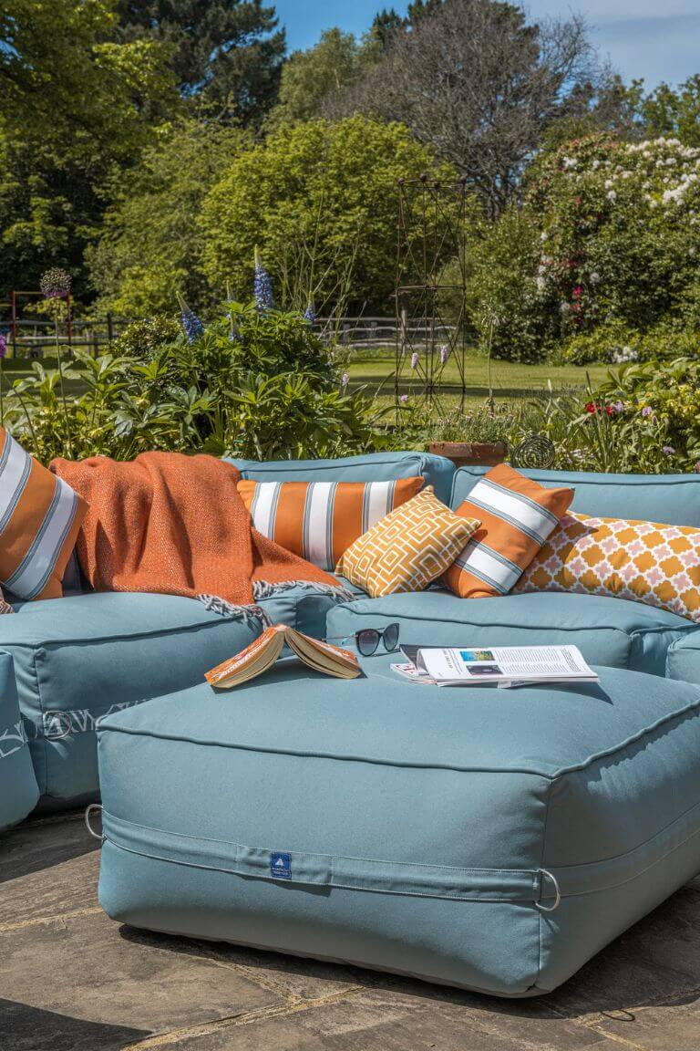 An ocean blue garden sofa is decorated with bright orange striped outdoor scatter cushions