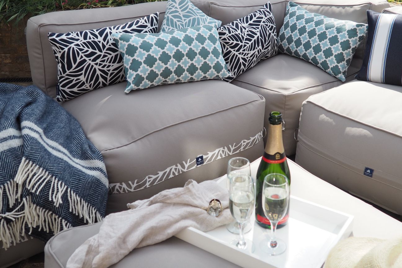 A high end bean bag outdoor sofa and blue patterned garden cushions with a bottle of champagne on a weatherproof ottoman