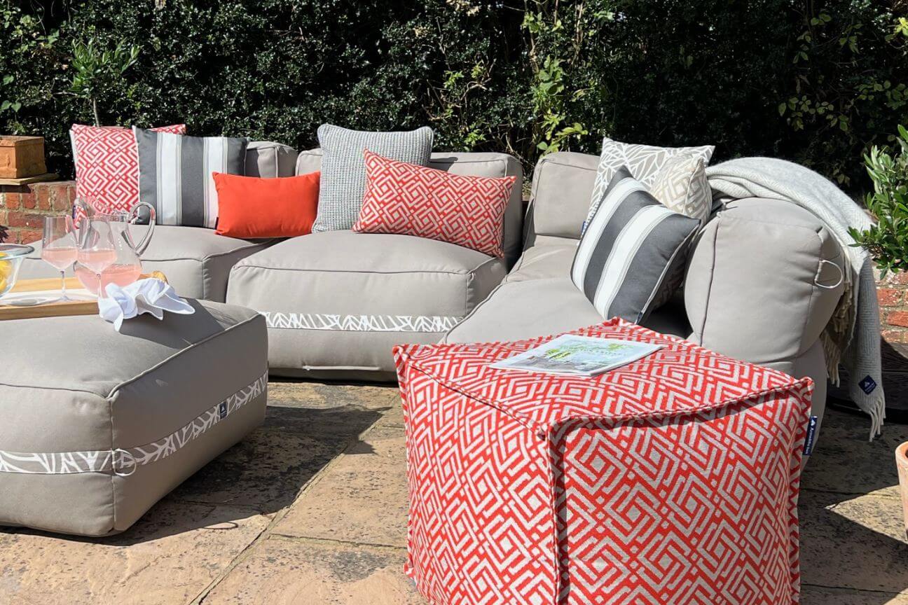 A modular garden sofa covered with grey striped and red-patterned cushions