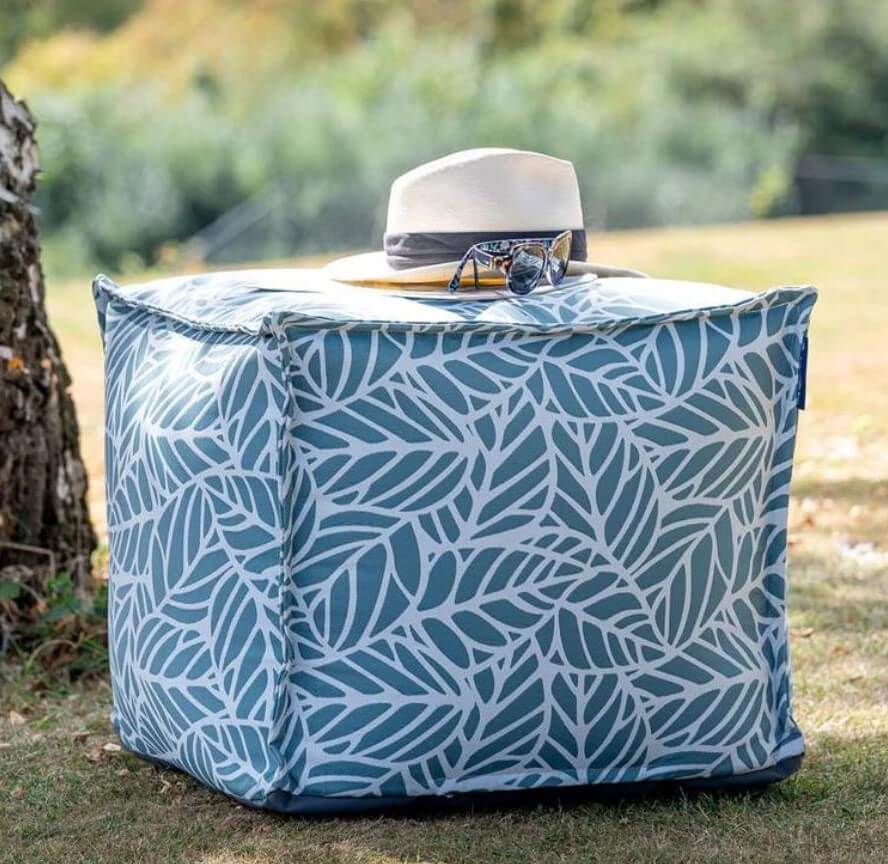 A cube-shaped outdoor pouffe made from ocean blue fabric with a palm-leaf print