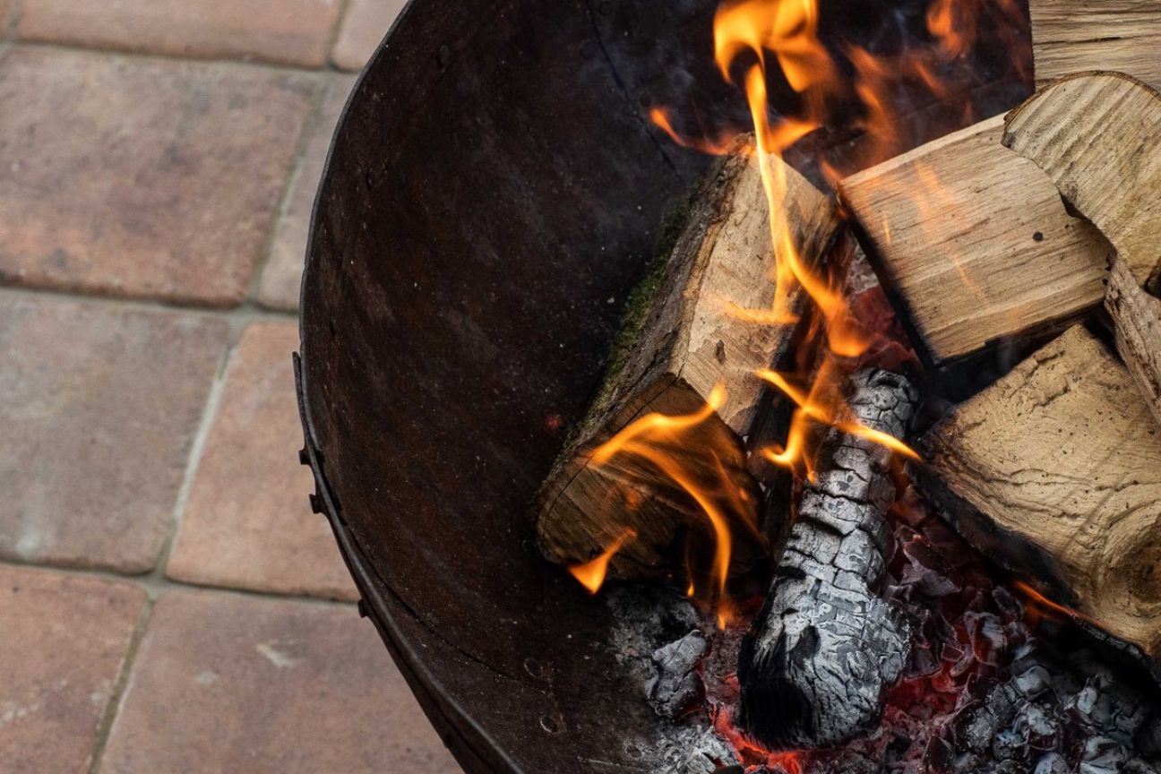 Fire pit filled with burning logs on a terracotta coloured tiled patio