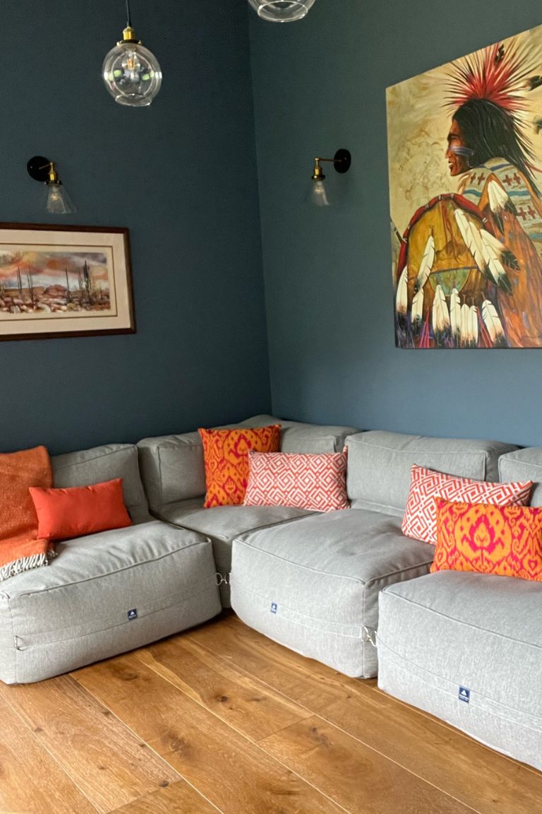 A large light grey cushiony sofa in the corner of a dark blue painted room.