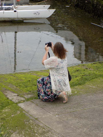 Woman kneeling on Polperro Harbour walkway, taking a photo of the boats 
