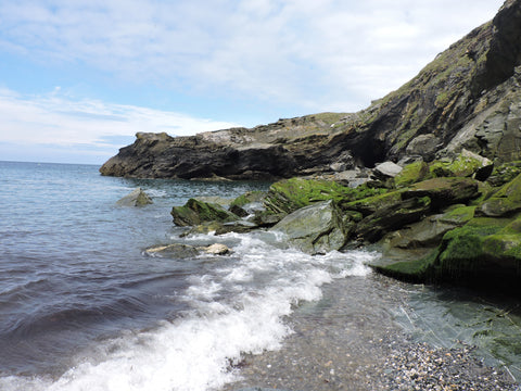 View of Tintagel Beach with sea to the left and mossy green cliffs to the right