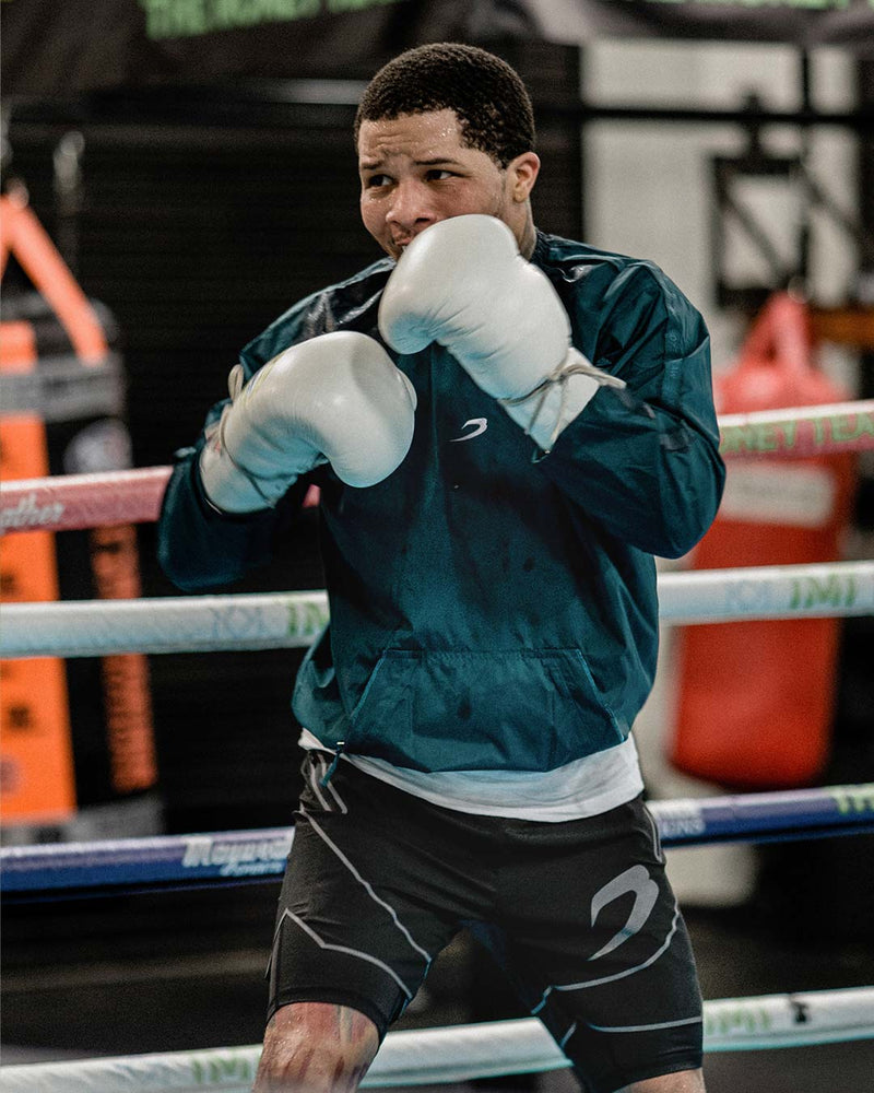 Man in a green sauna suit tracksuit with a white boxraw logo on the chest as well as adjustable wrist straps and made from polyester.