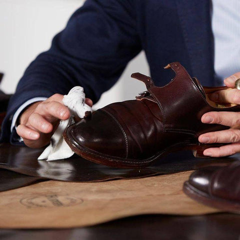 person using a damp cloth to remove a stain from a brown leather boot.