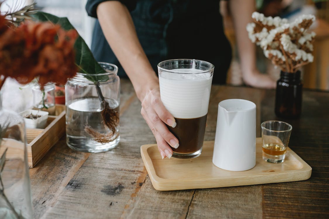 Crop unrecognizable woman serving iced chocolate coffee on tray