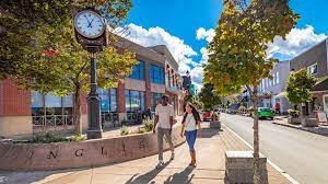 A view of Inglis Place, a street in Downtown Truro, with two people walking by the clock at the corner of the street. 