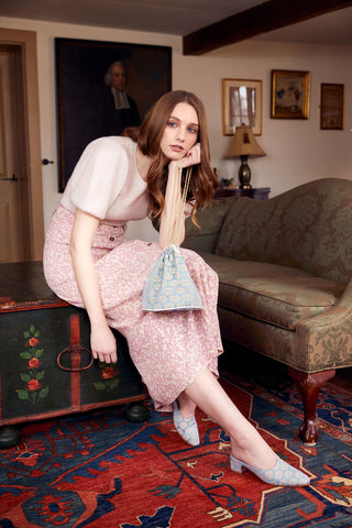 woman-sitting-on-coffee-table-wearing-lyon-moss-mules-and-holding-drawstring-pouch