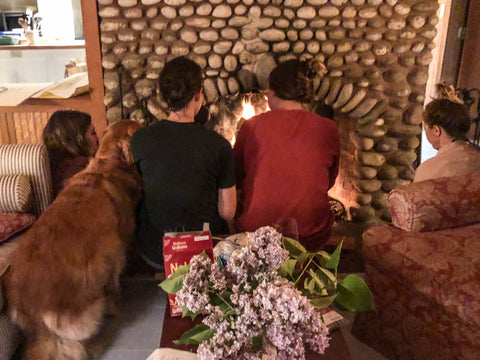 Lena, McNeill and Carson sitting toward stone surrounded fireplace with purple flowers behind them. 