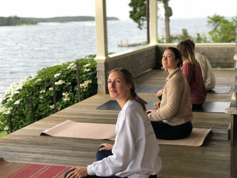 Milicent, McNeill and Carson sitting waterside preparing for yoga. 