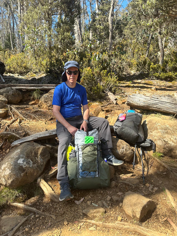 A hiker seated on a boulder, wearing a backpack, surrounded by a serene natural landscape