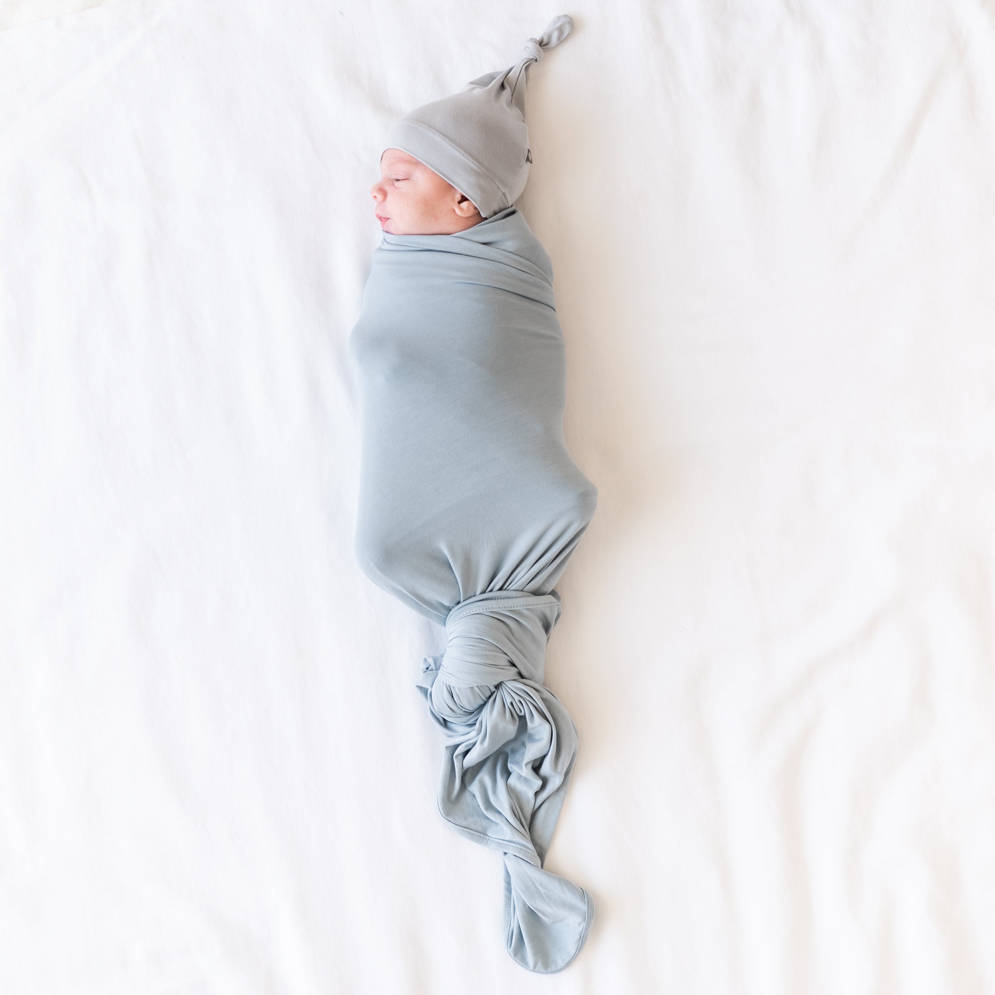 Baby being swaddled in blue grey swaddle and grey hat