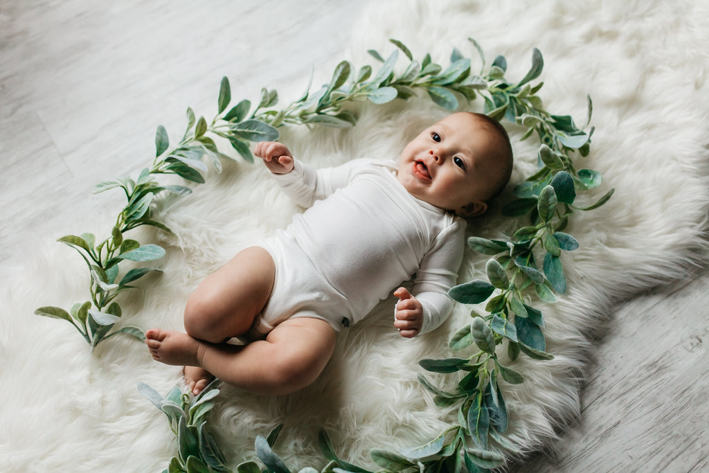 happy baby in a bamboo bodysuit with green garland