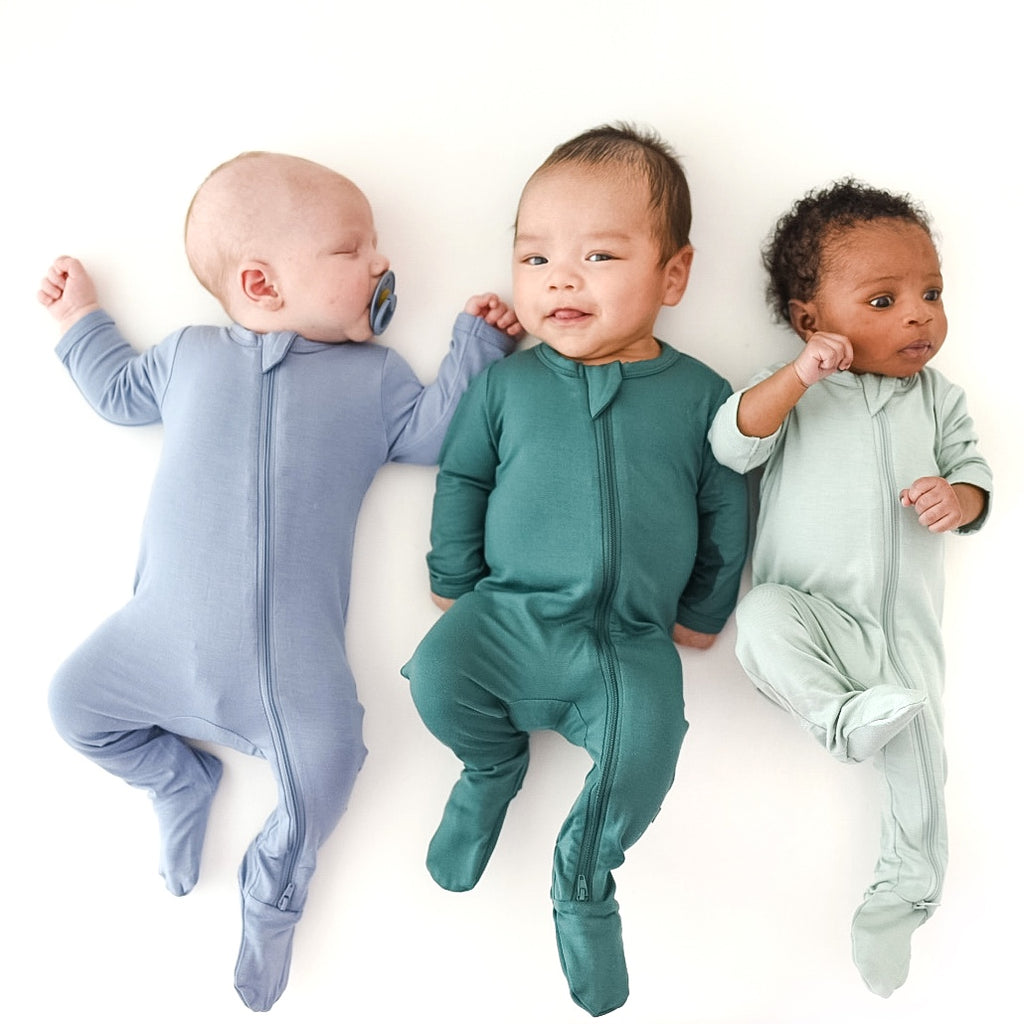 Three newborns laying down side by side in neutral bamboo pajamas