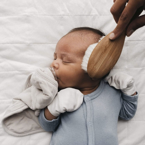 sleeping baby whose hair is being brushed with a kyte baby cradle cap brush