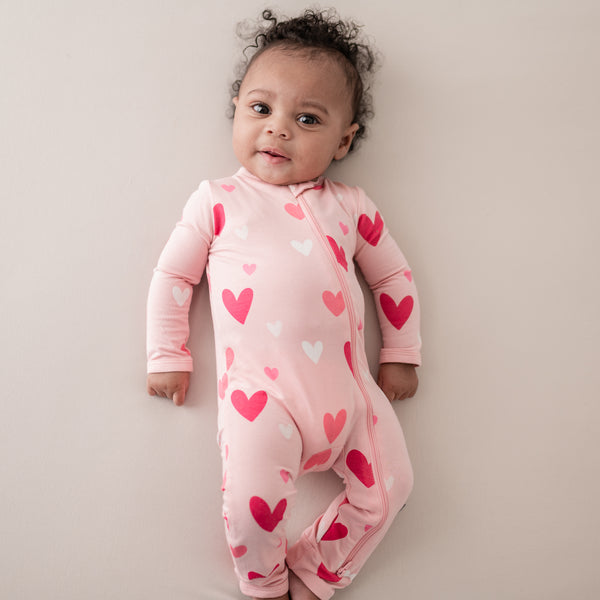 baby wearing a kyte baby romper in crepe hearts print