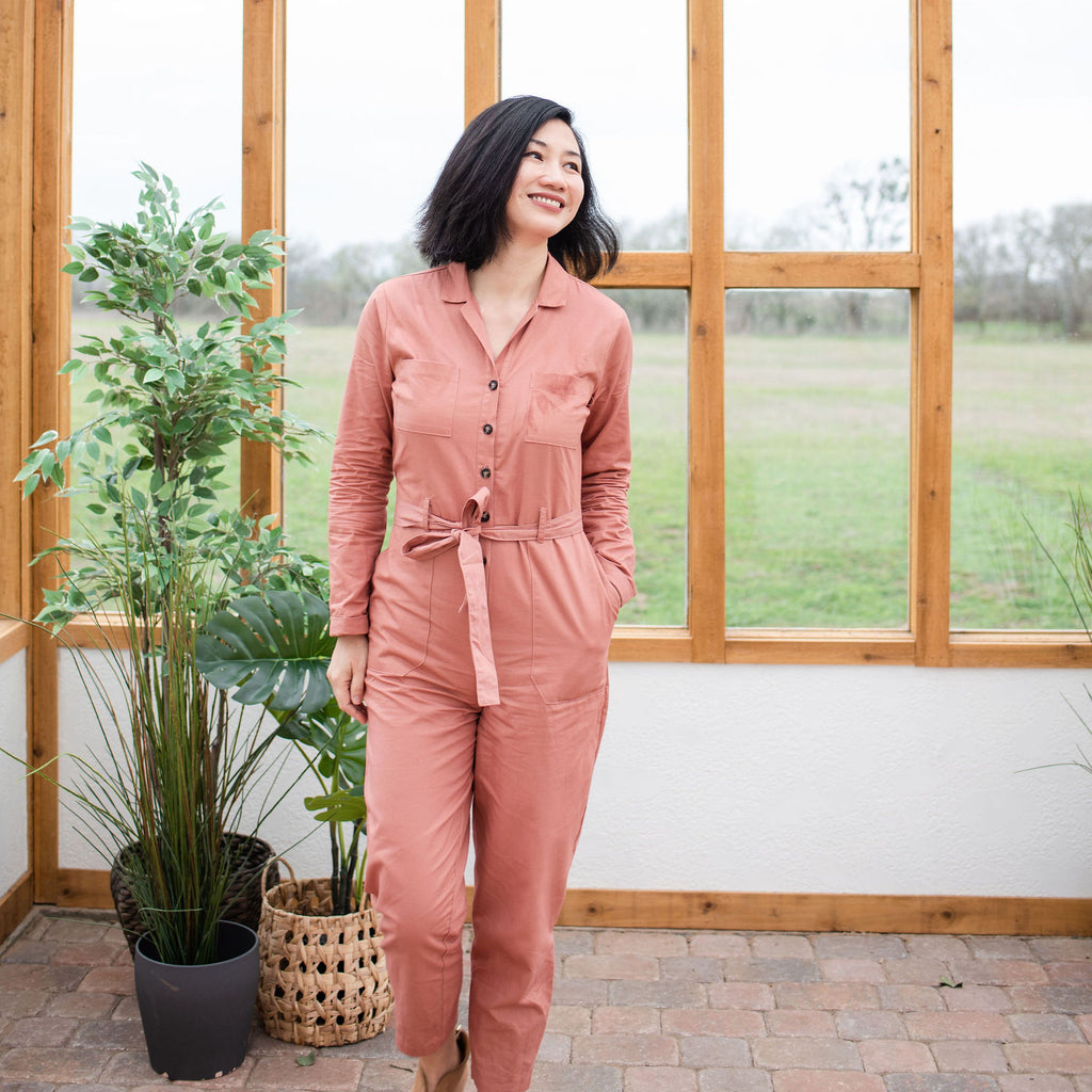 asian woman walking with one hand in pocket wearing pink inside a greenhouse