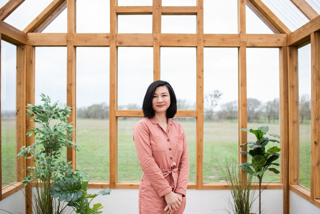 Asian woman standing in a greenhouse wearing a pink jumpsuit