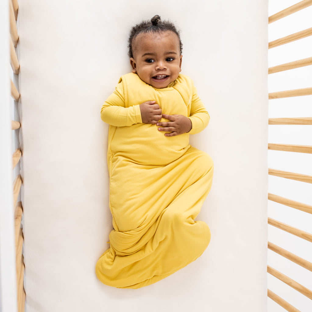 Baby smiling in crib with a yellow sleep bag on color is "Pineapple"