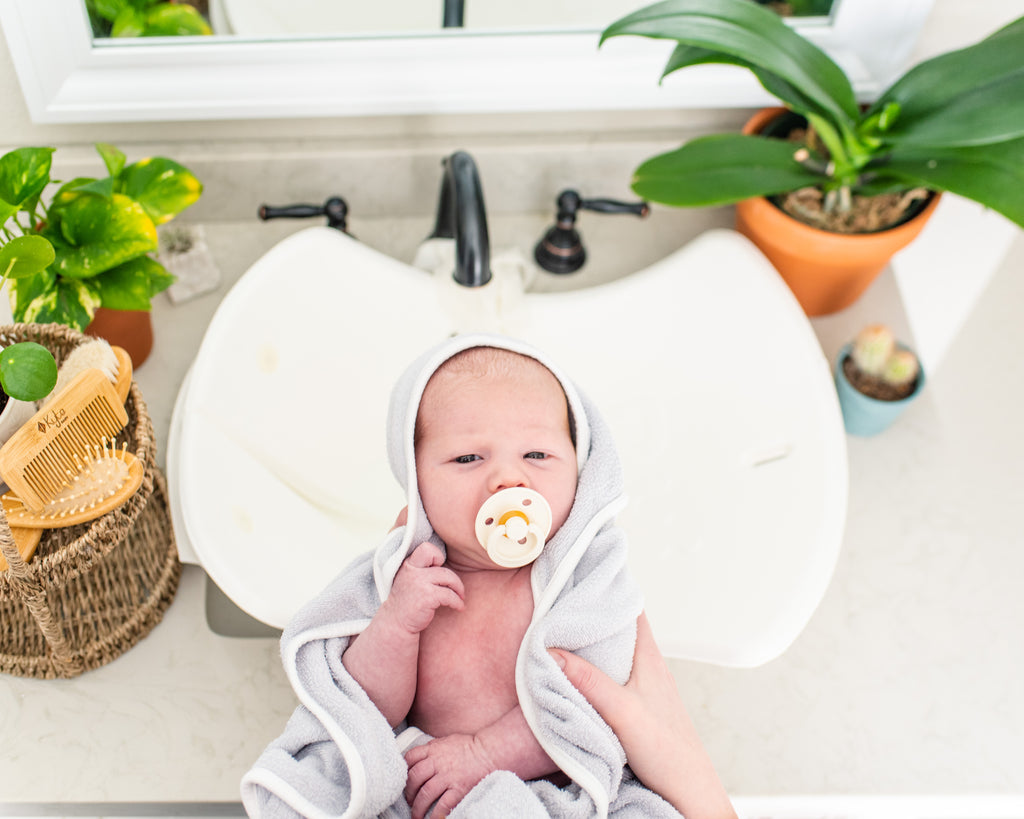 baby wrapped in towel with paci in mouth above bathroom sink