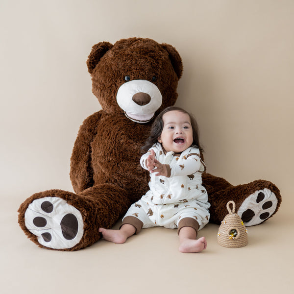 baby wearing a kyte baby sleep bag swaddler in honey bear print with a giant stuffed teddy bear