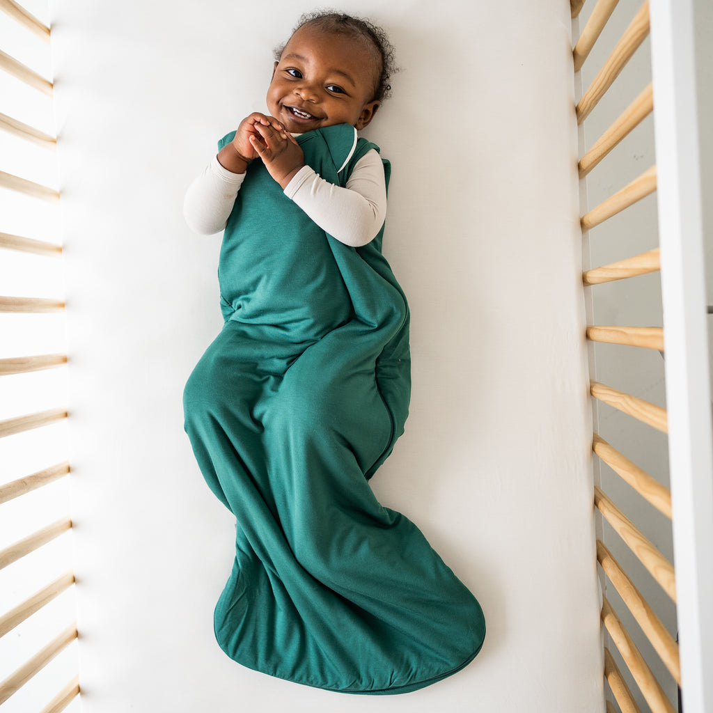 baby in green sleep bag smiling looking at camera