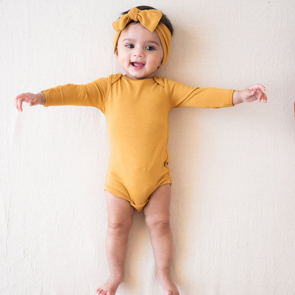 baby laying down and wearing a kyte baby long sleeve bodysuit and bow