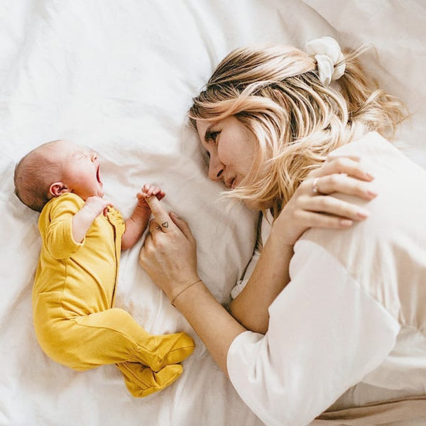 New mother holding newborn's hand while laying on the bed