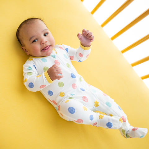 baby laying in crib and wearing a kyte baby footie in spring egg print