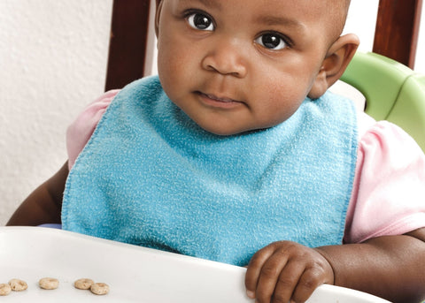 baby eating cheerios in high chair