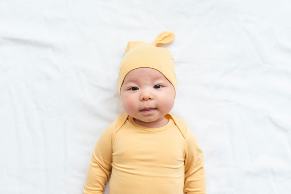 baby wearing kyte baby knotted cap and bodysuit smiling at camera