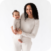 Mother wearing matching pajamas holding here baby smiling at the camera