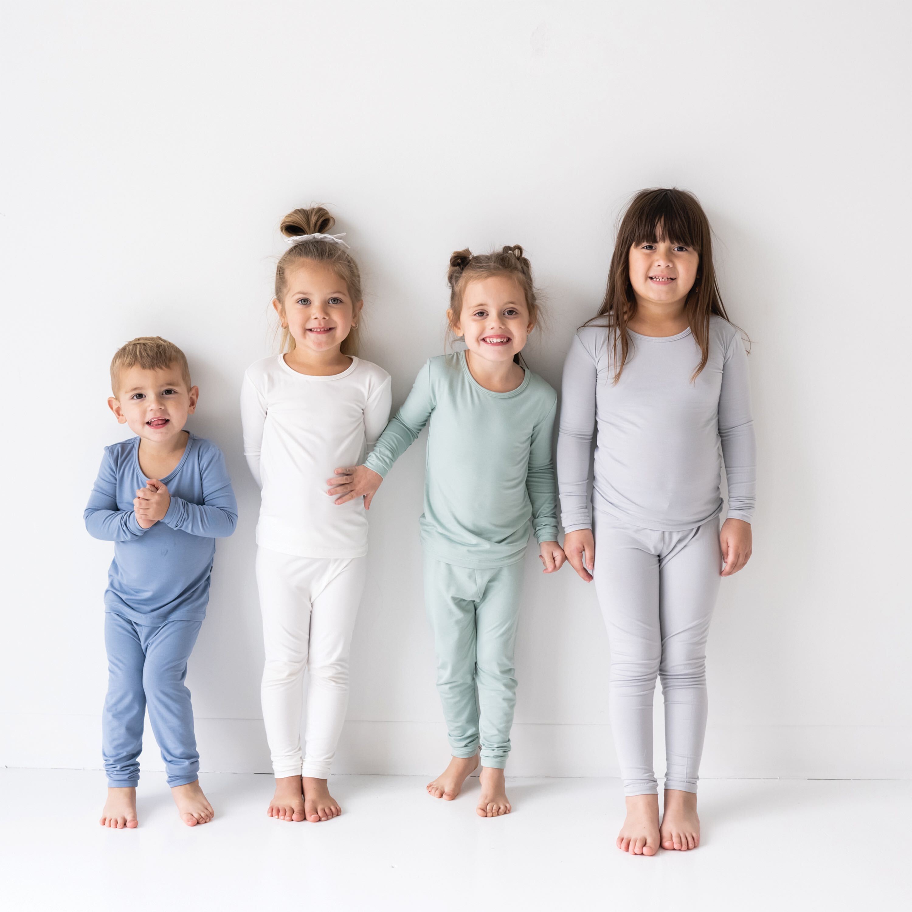 Four children wearing Kyte pajamas standing against a wall smiling for the camera