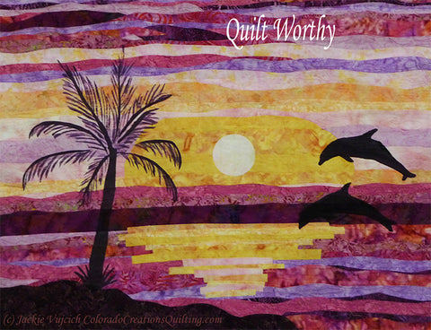 Dancing Dolphins quilt by Colorado Creations Quilting features dolphins jumping out of the water with a sunset in the background and a silhouette of a palm tree on shore.