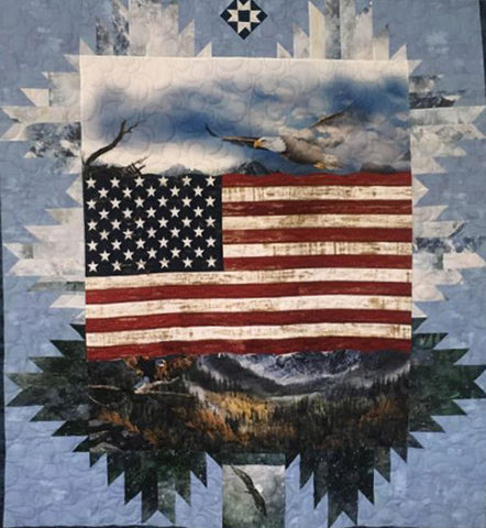 The quilt features the United States flag surrounded by bald eagles flying in a blue sky and green mountains below.
