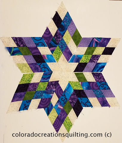 A quilt with a 6-pointed star in the center which is made of diamonds in cream, blue, purple and green made by Jackie Vujcich of Colorado Creations Quilting.