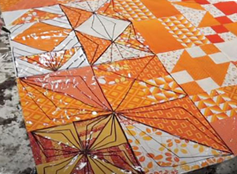 An orange and white quilt top with a plastic vinyl table cover placed on top.  