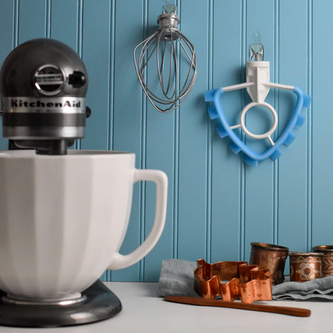 SideSwipe beater and whisk hanging on blue wall behind KitchenAid stand mixer