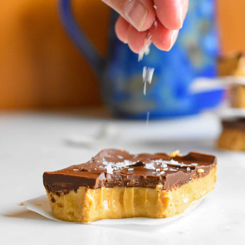 hand sprinkling coarse salt on chocolate peanut butter bars