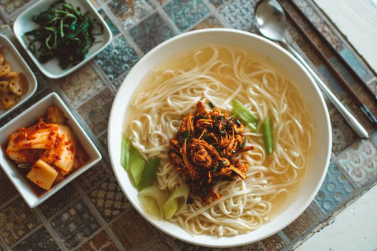 Un bol de soupe coréenne avec du panchan ou des accompagnements à gauche du bol et une soupe et des baguettes à droite du bol.