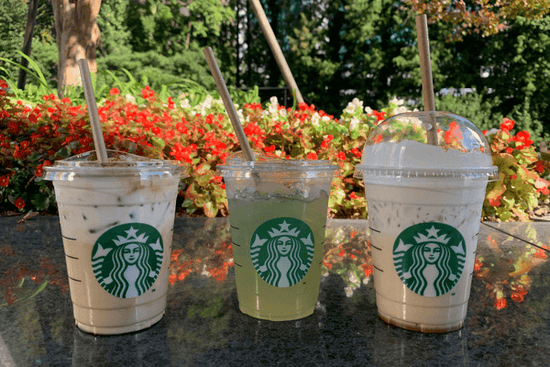 Tres bebidas de café Starbucks con follaje rojo, amarillo y blanco en el fondo.