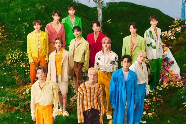 Seventeen members wearing colorful outfits surrounded by flowers