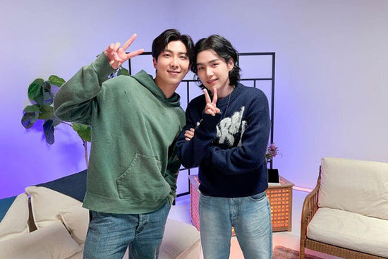 Les membres de BTS RM et Suga posant pour une photo sur le tournage de son nouveau talk-show de consommation de consommation de talk-show telwita, tous deux en tenant des panneaux de paix. 