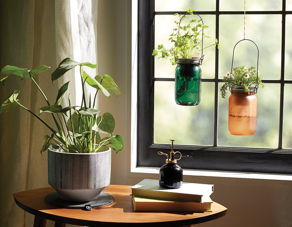 Two Modern Sprout garden jars hanging in window next to an end table with a book and plant