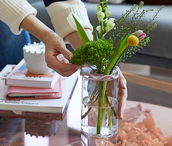 two hands arranging a Modern Sprout Botanical keeper and a vase of flowers and greenery
