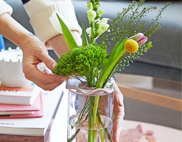 two hands touching a flower arrangement in a glass jar on top of a coffee table